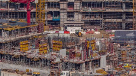 Téléchargez les photos : Grand chantier de construction avec de nombreuses grues de travail timelapse. Vue aérienne du grand développement du quartier résidentiel et de bureaux à Business Bay, Dubaï. Bulldozer et camion - en image libre de droit