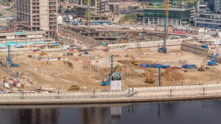 Foto de Conducción de pilotes en foso de cimentación para la construcción del edificio de apartamentos timelapse aéreo. Instalación profunda y excavación con maquinaria pesada como excavadora, grúas, excavadoras y camiones, Dubai - Imagen libre de derechos