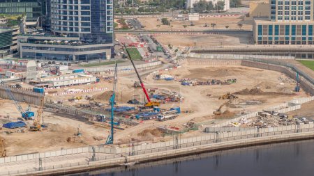 Téléchargez les photos : Pilotage de pieux dans la fosse de fondation pour la construction d'immeubles complexes d'appartements timelapse aérienne. Installation profonde et excavation avec pelles, grues, bulldozers et camions, Dubai Business Bay - en image libre de droit
