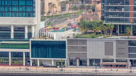 Foto de Paseo marítimo a lo largo del canal de agua en el distrito de Business Bay Dubai timelapse aéreo. Piscina en la azotea y restaurantes. Puentes sobre ribera con rascacielos desde arriba, Emiratos Árabes Unidos - Imagen libre de derechos