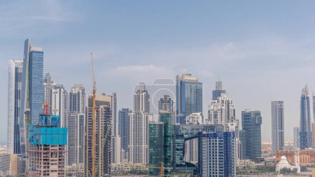 Téléchargez les photos : Paysage urbain avec les gratte-ciel de Dubai Business Bay et le canal d'eau timelapse aérien. Skyline moderne avec des tours résidentielles et de bureaux près de la mosquée. Chantier de construction du nouveau bloc. - en image libre de droit