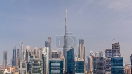 Téléchargez les photos : Vue aérienne vers Dubai Business Bay et le centre-ville avec les différents gratte-ciel et tours le long du front de mer sur le canal timelapse. Site de construction avec grues. Ciel nuageux toute la journée - en image libre de droit