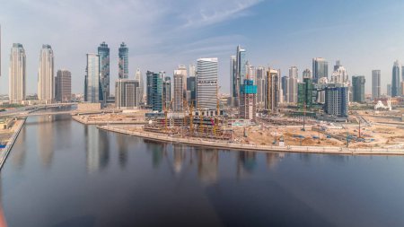 Foto de Paisaje urbano con rascacielos de Dubai Business Bay y timelapse aéreo del canal de agua. skyline moderno con torres residenciales y de oficina en el paseo marítimo. Gran obra de construcción. Nubes en un cielo azul - Imagen libre de derechos