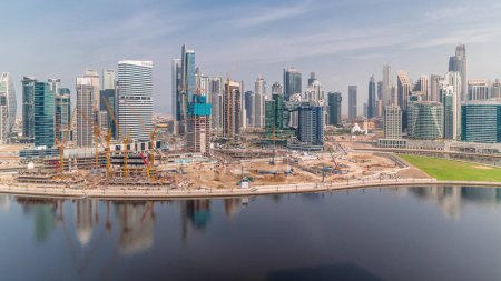 Photo for Cityscape panorama with skyscrapers of Dubai Business Bay and water canal aerial timelapse. Modern skyline with residential and office towers on waterfront. Cranes on a construction site of new block - Royalty Free Image