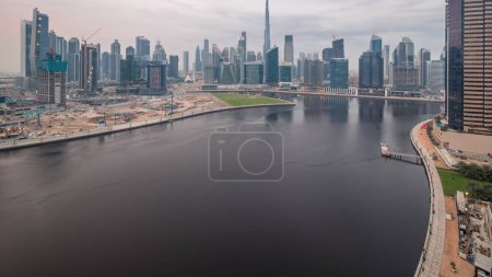 Téléchargez les photos : Skyline panoramique aérien Dubai Business Bay et Downtown avec les différents gratte-ciels et tours le long du front de mer sur le canal de jour à la transition nocturne timelapse. Site de construction avec grues après le coucher du soleil - en image libre de droit