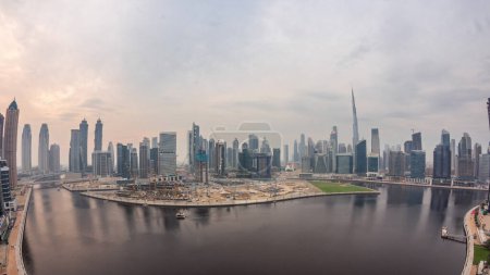 Foto de Vista aérea de Dubai Business Bay y el centro con los rascacielos y torres panorámicos a lo largo de la costa en el canal de día a noche timelapse transición. Lugar de construcción con grúas después del atardecer - Imagen libre de derechos