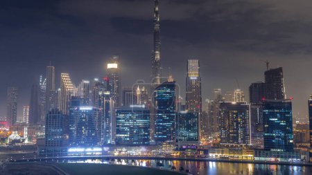 Foto de Vista aérea de Dubai Business Bay y el centro de la ciudad con los diversos rascacielos y torres a lo largo de la costa en la noche del canal timelapse. Espectáculo de luz y láser. Construcción con grúas - Imagen libre de derechos