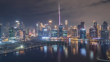 Foto de Vista panorámica aérea de Dubai Business Bay y el centro con varios rascacielos y torres a lo largo de la costa en la noche del canal timelapse durante toda la noche. Planta de construcción con grúas. Luces intermitentes - Imagen libre de derechos