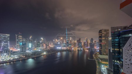Photo for Aerial view to Dubai Business Bay and Downtown with the various skyscrapers and towers covered by fog during all night. Waterfront and canal night timelapse. Construction site with cranes - Royalty Free Image