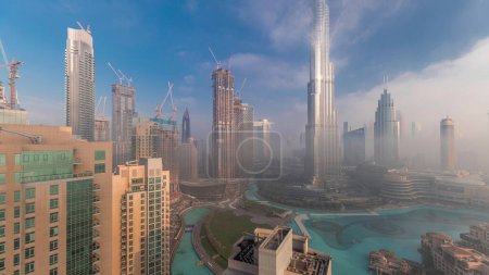 Téléchargez les photos : Vue aérienne de Dubaï tôt le matin pendant le brouillard. Lever de soleil à horizon futuriste de la ville avec des gratte-ciel et des tours d'en haut. Soleil réfléchi par la surface du verre avec des rayons de lumière - en image libre de droit