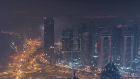 Photo for JLT and Dubai marina skyscrapers near Sheikh Zayed Road during all night aerial. Residential buildings and traffic on highway intersection. Lights tirning off - Royalty Free Image