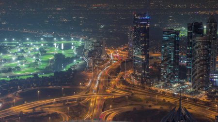 Foto de Gran cruce de caminos entre el distrito JLT y el puerto deportivo de Dubái intersecado por la transición día a noche de Sheikh Zayed Road. Tráfico de coches cerca de rascacielos iluminados - Imagen libre de derechos
