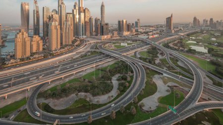 Photo for Panorama of Dubai Marina highway intersection spaghetti junction. Illuminated tallest skyscrapers and golf course on a background. Aerial top view from JLT district before sunrise - Royalty Free Image
