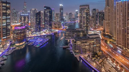 Téléchargez les photos : Vue aérienne vers les gratte-ciel de la marina de Dubaï et les tours jbr autour du canal avec des bateaux flottants transition jour-nuit. Les bateaux blancs sont garés dans le yacht club après le coucher du soleil - en image libre de droit