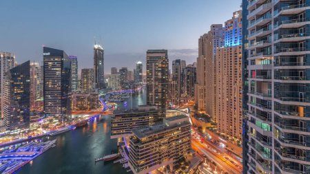 Téléchargez les photos : Vue aérienne des gratte-ciel de la marina de Dubaï autour du canal avec des bateaux flottants transition jour-nuit. Les bateaux blancs sont garés dans le yacht club après le coucher du soleil - en image libre de droit