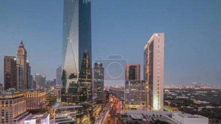Foto de Distrito financiero internacional de Dubái transición día a noche. Vista aérea panorámica de las torres de oficinas de negocios después del atardecer. Rascacielos con hoteles y tráfico en una carretera cerca del centro - Imagen libre de derechos