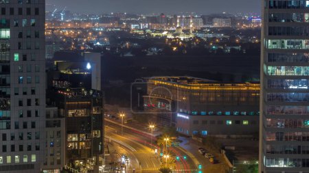 Foto de Vista panorámica del tráfico en la calle Al Saada cerca del distrito DIFC durante toda la noche y el distrito Deira en un segundo plano en Dubai, Emiratos Árabes Unidos. Rascacielos en vista aérea del centro financiero desde arriba. Ventanas brillantes - Imagen libre de derechos