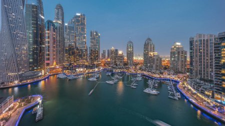Téléchargez les photos : Dubai marina gratte-ciel les plus hauts et les yachts dans le port aérien transition de jour à la nuit après le coucher du soleil. Vue sur les immeubles d'appartements, les hôtels et les immeubles de bureaux, développement résidentiel moderne des EAU - en image libre de droit
