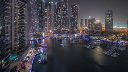 Téléchargez les photos : Panorama showing luxury yacht bay in the city aerial night in Dubai marina. Modern skyscrapers along waterfront promenade and boats floating in harbor - en image libre de droit