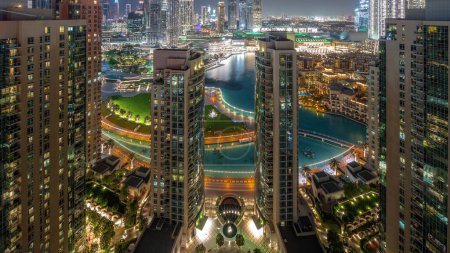 Téléchargez les photos : Dubaï Paysage urbain du centre-ville avec les plus hauts gratte-ciel autour de la fontaine transition aérienne du jour à la nuit. Parc avec lac et zone de marche d'en haut - en image libre de droit