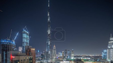 Foto de Panorama showing aerial cityscape night with illuminated architecture of Dubai downtown. Many tall skyscrapers and towers with glowing windows. New construction site. - Imagen libre de derechos