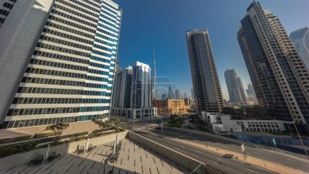 Foto de Vista panorámica aérea hacia el centro de Dubái y dic rascacielos durante el amanecer con tráfico ocupado en la intersección en el distrito de Business Bay. Sol reflejado desde la superficie de vidrio en las torres - Imagen libre de derechos