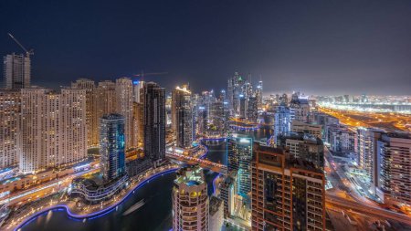 Téléchargez les photos : Panorama de divers gratte-ciel dans le plus haut bloc recidential de Dubai Marina transition aérienne de jour à la nuit avec canal artificiel. Nombreuses tours dans le quartier JBR et yachts après le coucher du soleil - en image libre de droit