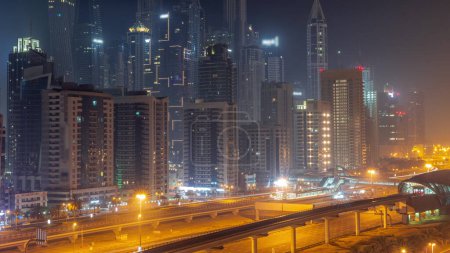 Téléchargez les photos : Dubai Marina plus grand bloc de gratte-ciel pendant toute la nuit avec des lumières éteintes. Vue aérienne du quartier JLT vers les immeubles à appartements, les hôtels et les tours de bureaux près de l'autoroute. - en image libre de droit