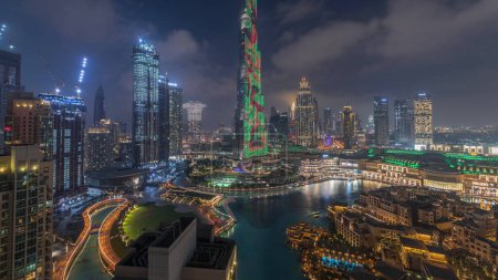 Foto de Rascacielos que se elevan por encima del centro de Dubái transición día a noche, centro comercial y fuente rodeada de edificios modernos vista panorámica superior aérea con cielo nublado colorido - Imagen libre de derechos