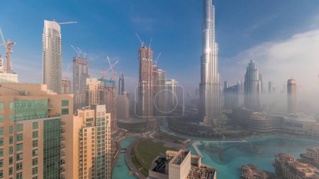 Foto de Vista aérea de la ciudad de Dubai temprano en la mañana durante la niebla. Salida del sol en el horizonte futurista de la ciudad con rascacielos y torres desde arriba. Sol reflejado desde la superficie de vidrio con rayos de luz - Imagen libre de derechos