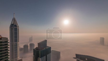 Téléchargez les photos : Lever du soleil sur un brouillard hivernal rare tôt le matin au-dessus des toits de la marina de Dubaï et des gratte-ciel aériens. Vue de dessus depuis les nuages. Dubai, Émirats arabes unis - en image libre de droit