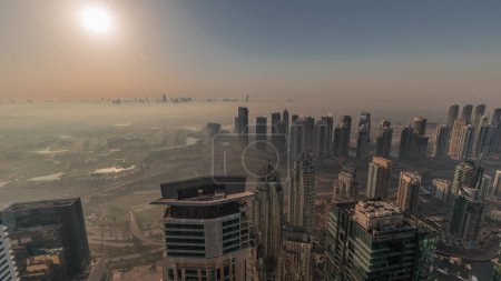 Photo for Panorama of Dubai Marina with JLT skyscrapers and golf course during sunrise, Dubai, United Arab Emirates. Aerial view from above towers foggy morning. City skyline with orange sky - Royalty Free Image