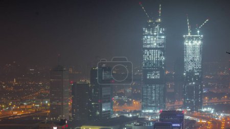 Téléchargez les photos : Vue aérienne de gratte-ciel éclairés avec World Trade Center à Dubaï toute la nuit avec des lumières éteintes. Site de construction de nouvelles tours jumelles. Bur Dubai et le district de Deira sur un fond - en image libre de droit