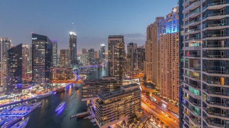 Photo for Aerial view to Dubai marina skyscrapers around canal with floating boats day to night transition. White boats are parked in yacht club after sunset - Royalty Free Image