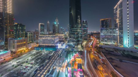 Foto de Distrito financiero internacional de Dubái transición día a noche. Vista aérea panorámica del estacionamiento y las torres de oficinas de negocios después del atardecer. Rascacielos con hoteles y centros comerciales cerca del centro - Imagen libre de derechos