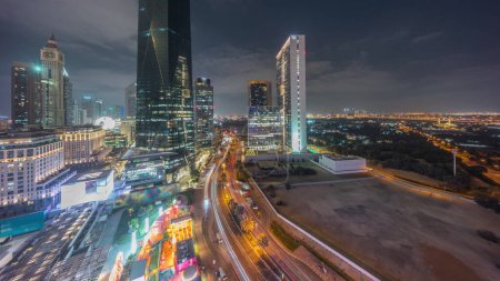 Téléchargez les photos : Dubai International Quartier financier transition jour-nuit avec la circulation dans une rue. Vue aérienne panoramique des tours de bureaux d'affaires après le coucher du soleil. gratte-ciel près du centre ville - en image libre de droit