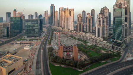 Foto de Bay Avenue con torres modernas desarrollo residencial en Business Bay panorámica aérea de noche a día de transición, Dubai, Emiratos Árabes Unidos. Rascacielos con tráfico en una carretera cerca de un gran aparcamiento - Imagen libre de derechos