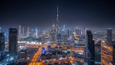 Panorama showing aerial view of tallest towers in Dubai Downtown skyline and highway night panorama. Financial district and business area in smart urban city. Skyscraper and high-rise buildings