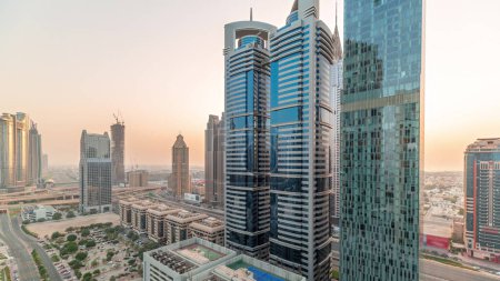 Téléchargez les photos : Panorama aérien du quartier financier international de Dubaï avec de nombreux gratte-ciel toute la journée avec des ombres se déplaçant rapidement. Trafic sur une route près d'un parking avec un court de tennis sur le toit. Dubai, Émirats arabes unis. - en image libre de droit