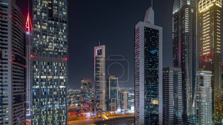 Photo for Panorama showing aerial view of Dubai International Financial District with many illuminated skyscrapers night. Traffic on a road near multi storey parkings. Dubai, UAE. - Royalty Free Image