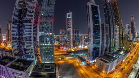 Foto de Panorama del Distrito Financiero Internacional de Dubai con muchos rascacielos durante toda la noche aérea. Tráfico en una carretera y torres iluminadas con luces apagadas. Dubai, Emiratos Árabes Unidos. - Imagen libre de derechos