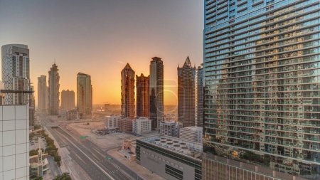 Foto de Skyline distrito de la bahía de negocios con la arquitectura moderna timelapse durante la puesta del sol desde arriba. Vista panorámica aérea de los rascacielos y torres de Dubái cerca de la carretera principal. Tráfico en una encrucijada - Imagen libre de derechos