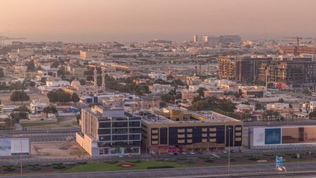Téléchargez les photos : Vue aérienne vers Dubai City Walk district timelapse. Nouvelle partie moderne avec des bâtiments de faible hauteur et des villas créées comme rues de style européen. Circulation sur une route Cheikh Zayed le soir avant le coucher du soleil - en image libre de droit