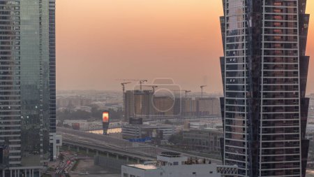 Foto de Sitio de construcción alrededor del canal de agua de Dubái con muchas grúas timelapse aéreo. Casas y villas están detrás de rascacielos de la bahía de negocios. Tráfico en el puente de la autopista. Cielo naranja al atardecer - Imagen libre de derechos