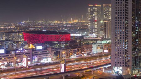 Téléchargez les photos : Vue aérienne vers Dubai City Walk district nuit timelapse. Nouvelle partie moderne avec des bâtiments de faible hauteur, arène et villas créées comme des rues de style européen. Grues de chantier et circulation sur l'autoroute - en image libre de droit