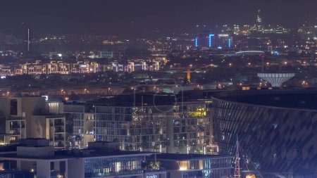 Téléchargez les photos : Vue aérienne rapprochée vers Dubai City Walk district nuit timelapse. Nouvelle partie moderne avec des bâtiments de faible hauteur et des villas créées comme rues de style européen. Rouge Illumination de l'arène éteinte - en image libre de droit