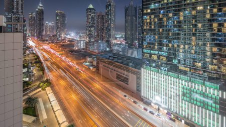 Foto de Skyline distrito de la bahía de negocios con la arquitectura moderna timelapse transición día a noche después de la puesta del sol desde arriba. Panorama aéreo de los rascacielos de Dubai, torres cerca de la carretera principal. Tráfico en encrucijada - Imagen libre de derechos
