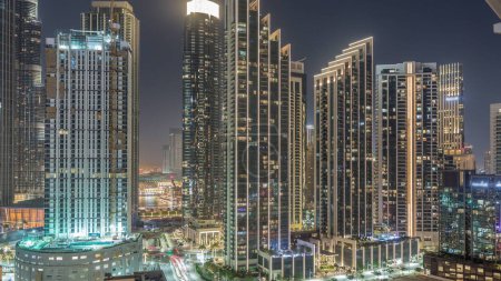 Foto de Vista aérea del horizonte del centro de Dubái con muchas torres iluminadas y fuente nocturna timelapse. Área de negocios en la ciudad urbana inteligente. Rascacielos y edificios de gran altura desde arriba, Emiratos Árabes Unidos. - Imagen libre de derechos