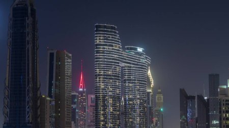 Téléchargez les photos : Tours futuristes et gratte-ciel éclairés avec des lumières dans les fenêtres à Dubaï Centre-ville et quartier financier. Urbain ville skyline aérienne nuit timelapse. Ciel noir - en image libre de droit