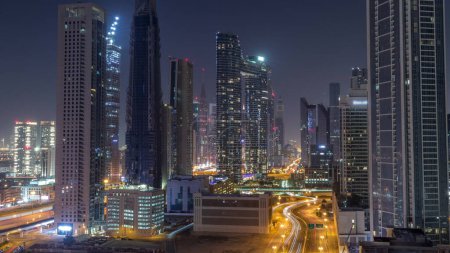 Foto de Torres futuristas y rascacielos iluminados con tráfico en las calles del centro de Dubái y distrito financiero con luces apagadas. Ciudad urbana skyline aérea durante toda la noche timelapse. - Imagen libre de derechos